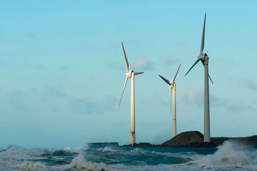 Three wind turbines on a coastal edge with waves crashing in front