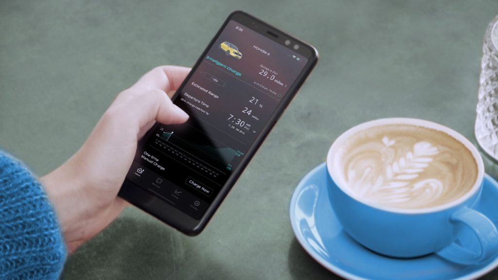 A hand holding a phone that shows the e:PROGRESS app on screen with a coffee in the background