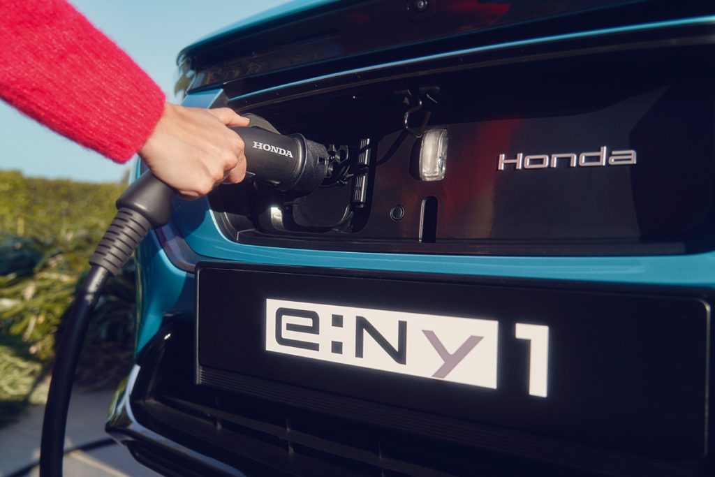 A close up front view of the charging point on a Honda e:Ny1 car with a hand plugging the charger into the car